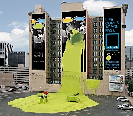 A billboard that spans the side of three buildings featuring a paint can that is spilling neon green paint. The building and parking lot beside the building are painted to look like the paint can spilled on them.